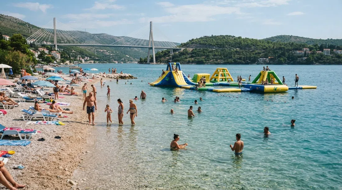 Playa Copacabana en Babin Kuk con aguas poco profundas, familias, el parque acuático hinchable Wibit flotante y el puente Franjo Tuđman al fondo