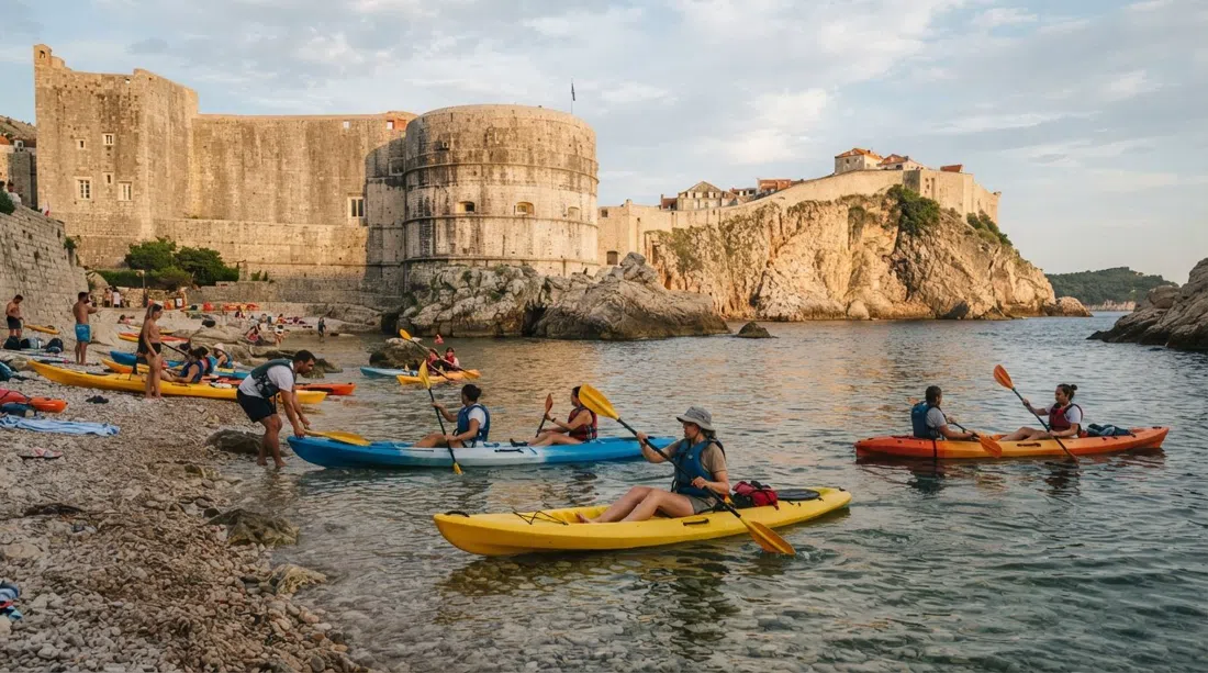 Kayaks de mar saliendo de la pequeña playa de Pile-Šulić, remeros dirigiéndose a lo largo de las murallas de la fortaleza al atardecer